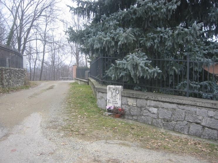 Cippo commemorativo a Varnà, incorniciato da piante e un sentiero che conduce verso un'area tranquilla.