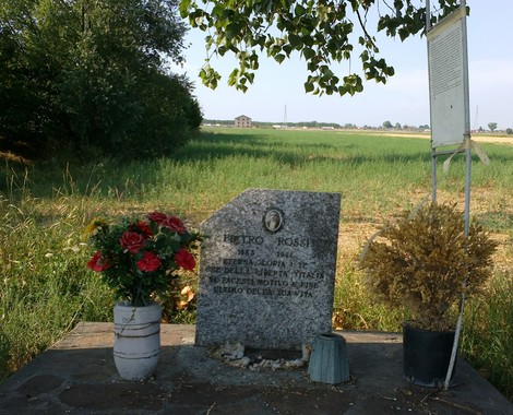 Cippo commemorativo a Rossi, con fiori e paesaggio verde, in memoria di eventi storici significativi.