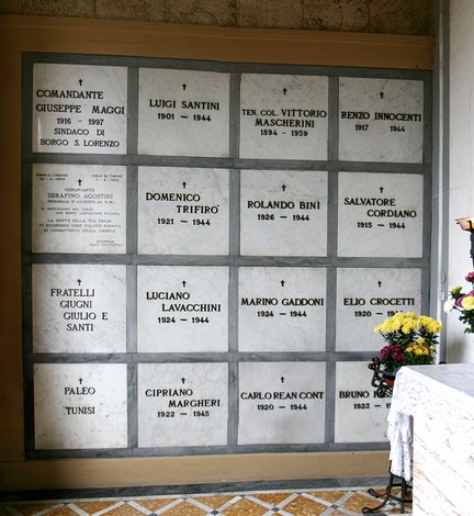 Sacrario dei partigiani con pannelli commemorativi in marmo e decorazioni floreali.