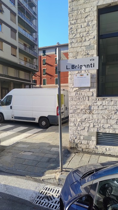 Targa stradale "via L. Briganti" su palo, davanti a un edificio in pietra all'angolo di una strada.