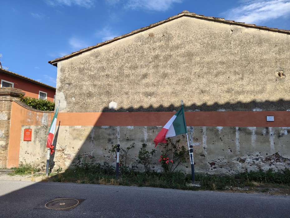 Muro della fucilazione dell'eccidio di Pettori, con bandiere italiane esposte e un ambiente rurale.