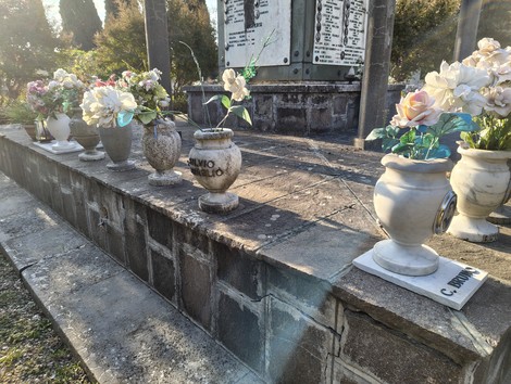 Sacrario ai caduti con vasi di fiori artificiale disposti ordinatamente su una base di pietra.