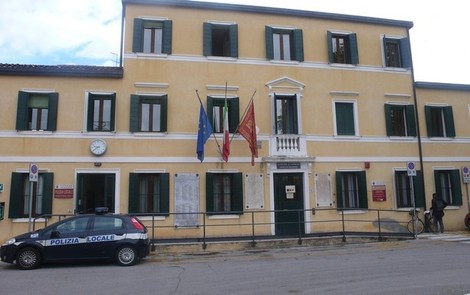 Edificio pubblico con facciata gialla, bandiere e auto della polizia locale parcheggiata.