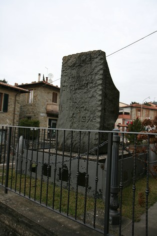 Monumento dei caduti, una stele commemorativa circondata da una recinzione in un contesto urbano.