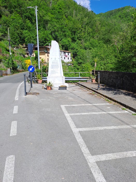 Monumento ai caduti di Guadine, situato lungo una strada in un'area verde e montuosa.