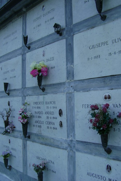 Sepolcri commemorativi dei caduti per la libertà, adornati con fiori e fotografie ricordo.