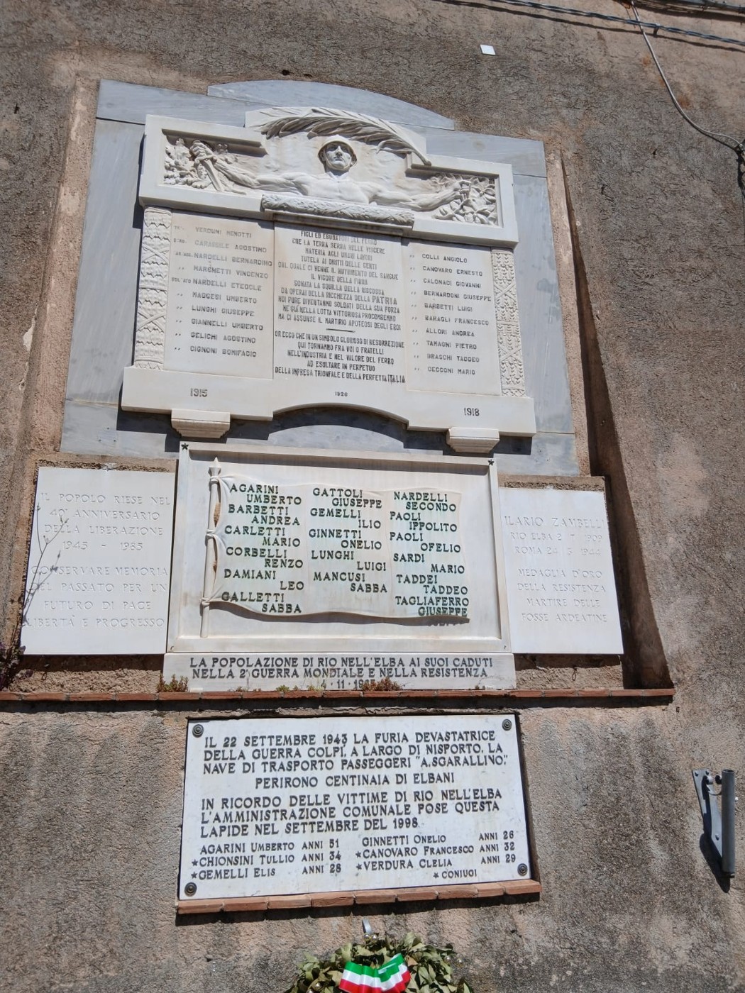Lapidi commemorative ai caduti di Rio nell'Elba, con iscrizioni e omaggi floreali.