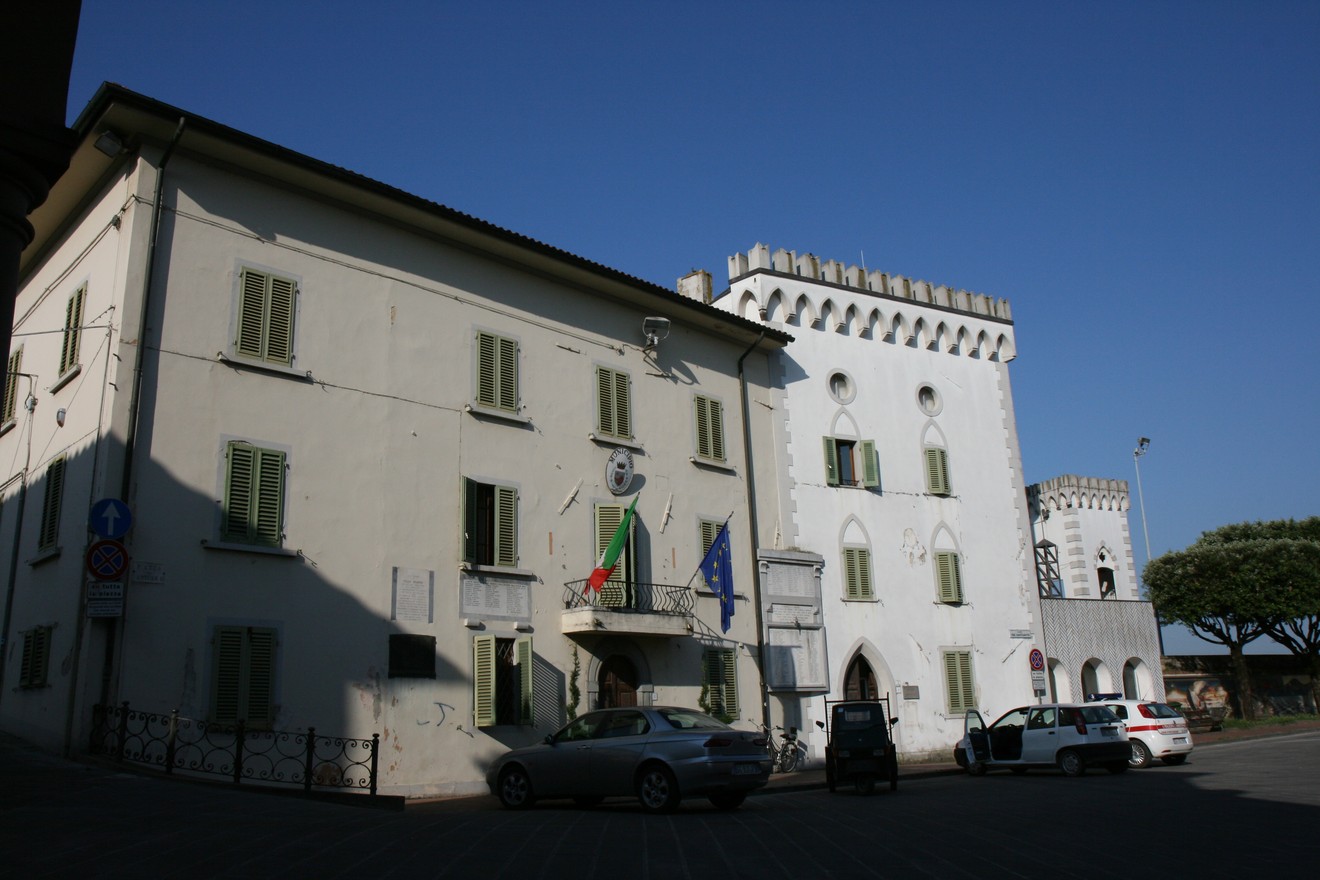 Lapide ai caduti civili, situata in una piazza con edifici storici e bandiere.