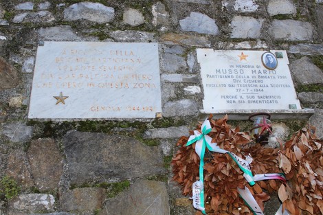 Lapide commemorativa di Musso con messaggi di ricordo e decorazioni floreali.