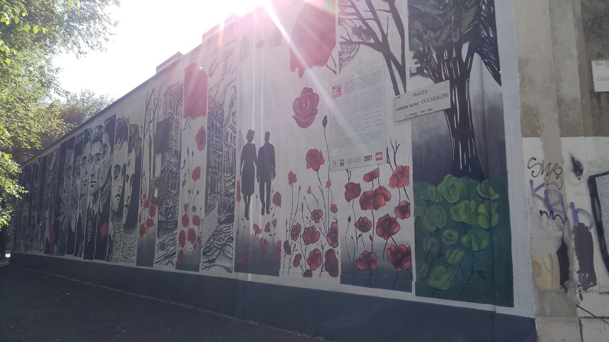 Murale dedicato ai Ragazzi di Via Botticelli, con figure stilizzate e fiori rossi su sfondo evocativo.