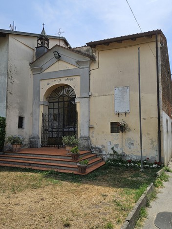 Lapide commemorativa situata accanto all'ingresso di un edificio, con piante e fiori decorativi.