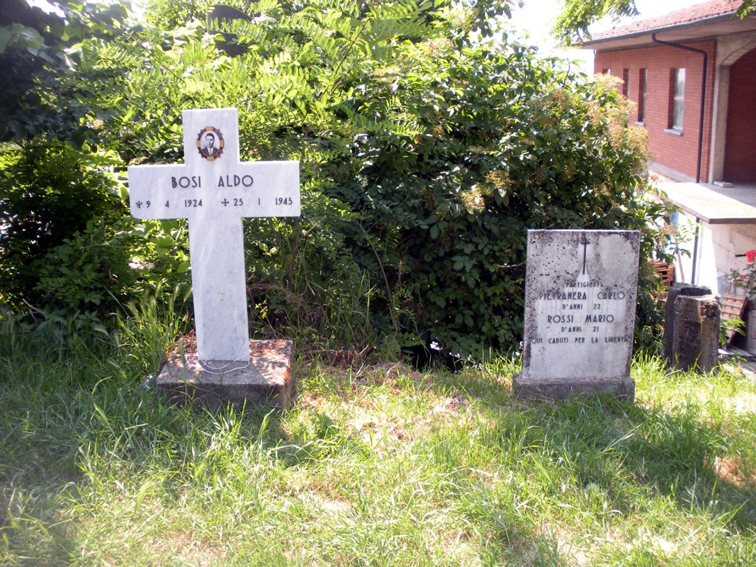 Lapide commemorativa di Aldo e Mario Rossi, con croce e pietra tombale in un'area verde.