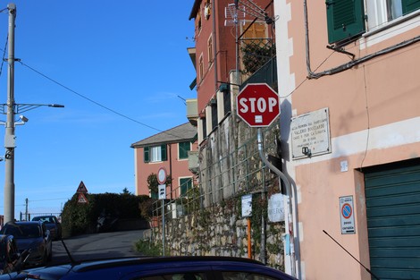 Lapide commemorativa e segnale di stop in un contesto urbano con edifici colorati e cielo azzurro.