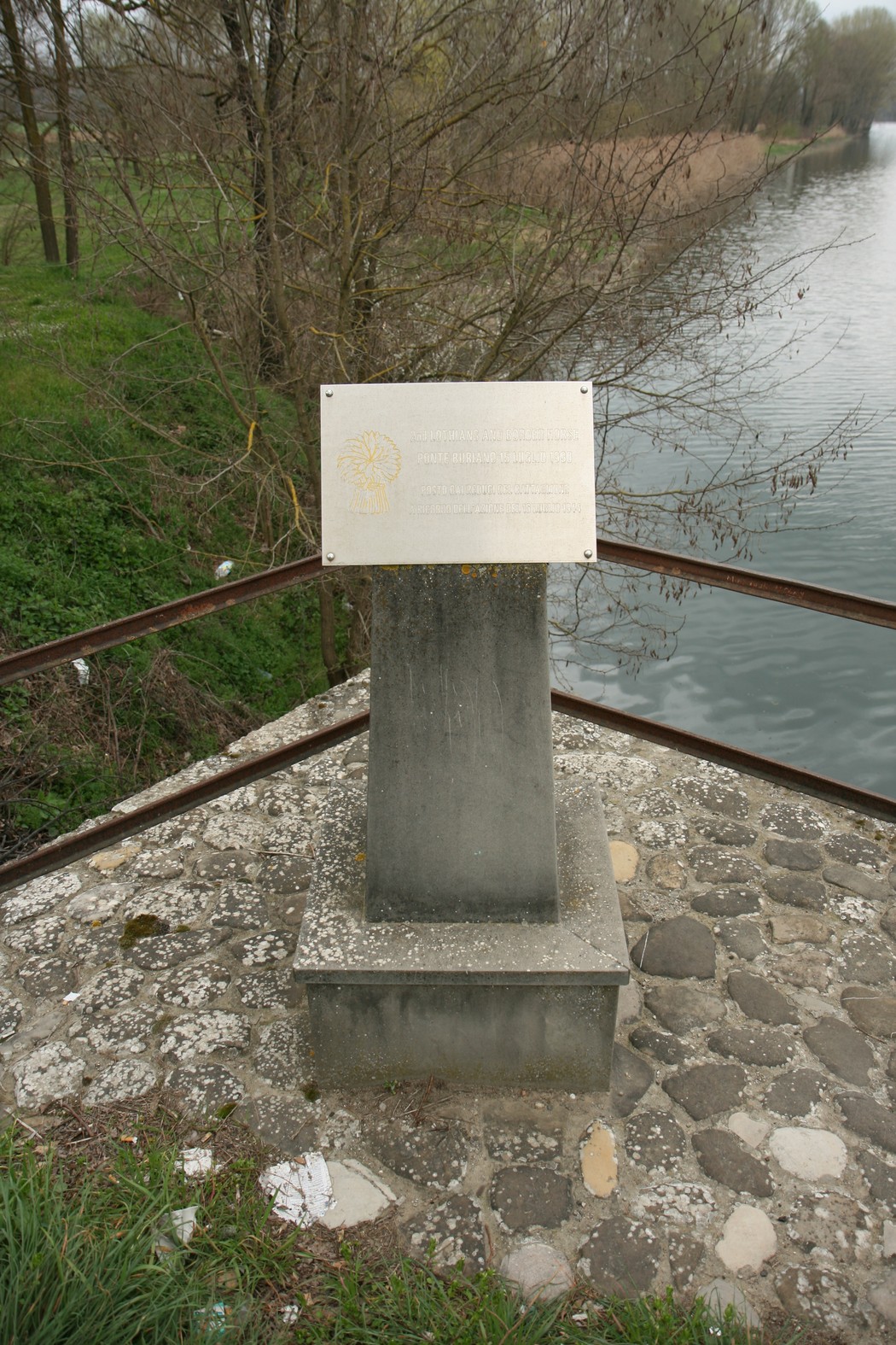 Cippo commemorativo del Secondo Battaglione Lothians, situato lungo un corso d'acqua, circondato dalla natura.
