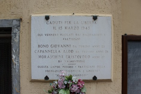 Lapide commemorativa in onore dei Martiri della Libertà, decorata con fiori, situata su un muro.