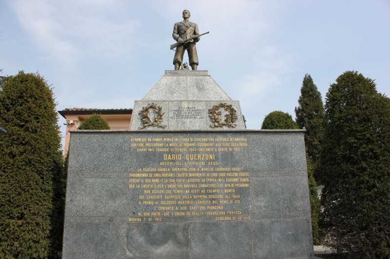 Monumento commemorativo a Guerzoni, con statua di un soldato e iscrizioni su base in marmo.