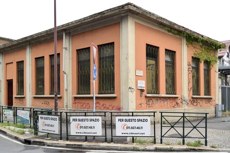 Lapide commemorativa a Prassuit su un edificio con graffiti e recinzione in un contesto urbano.