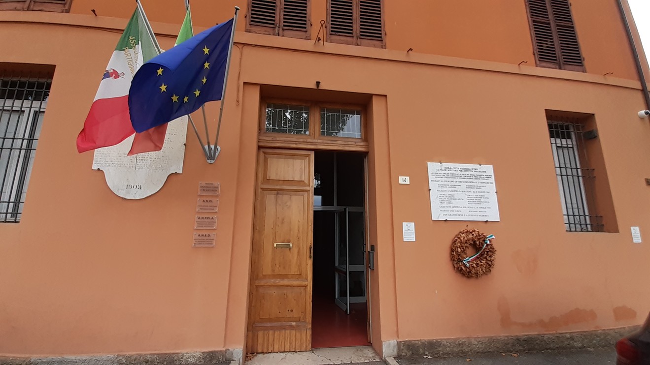 Lapide commemorativa dedicata ai partigiani imolesi caduti, situata a Bologna, con bandiere italiane ed europee.