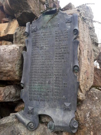 Monumento ai caduti, una scultura imponente con iscrizioni commemorative su fondo di pietra.