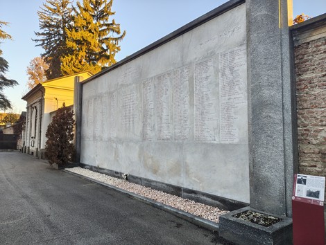 Sacrario dei deportati con un muro commemorativo che riporta nomi e date, immerso in un'atmosfera di rispetto e memoria.