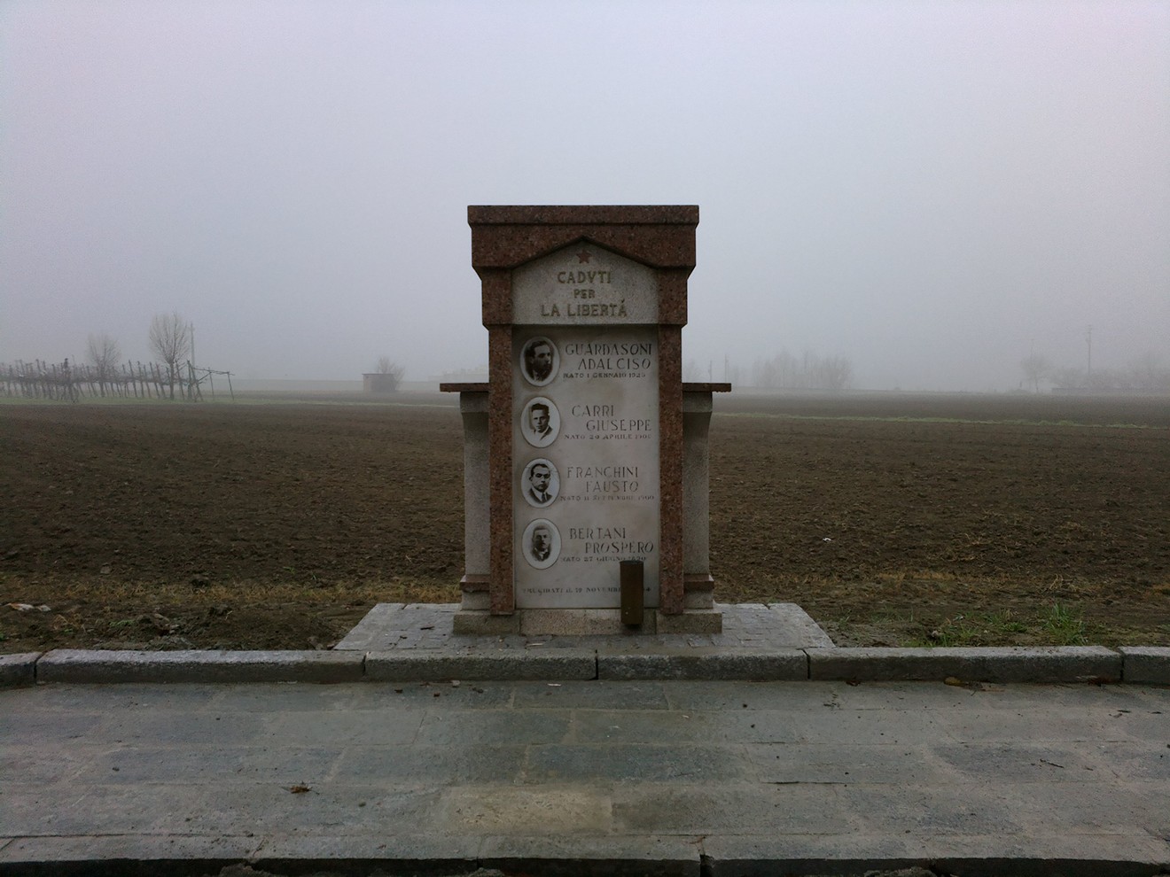 Monumento dedicato a Guardasoni, Carri, Franchini e Bertani, emblematico della libertà, in un paesaggio nebbioso.