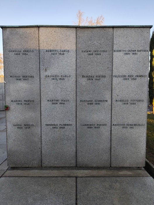 Monumento commemorativo in pietra con nomi incisi in memoria dei caduti. Atmosfera solenne e riflessiva.