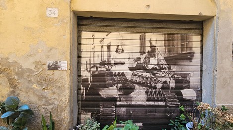 Murale che rappresenta una scena della sfilata di San Nicola su una saracinesca, con vegetazione circostante.
