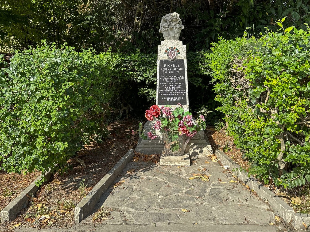 Monumento in memoria di Michele Morrone, circondato da piante e fiori, situato a Modena.