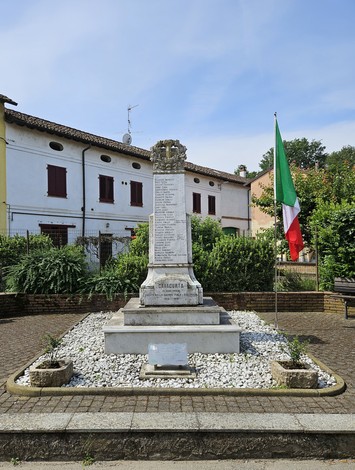 Monumento ai Caduti di Cavacurta, con bandiera italiana e circondato da aiuole e un pavimento di ciottoli.
