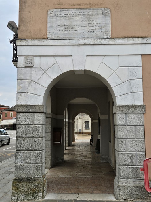 Lapide commemorativa in un portico, dedicata ai caduti per la liberazione, visibile su un muro.