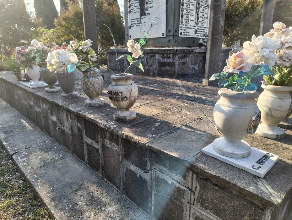 Sacrario ai caduti con vasi di fiori artificiale disposti ordinatamente su una base di pietra.