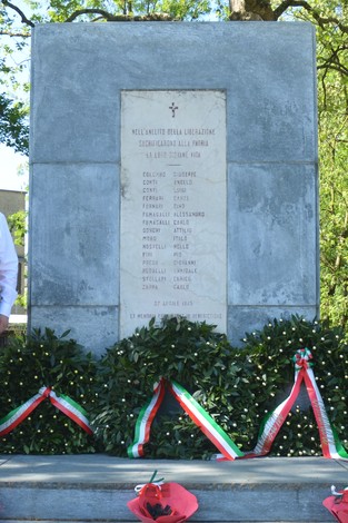 Monumento ai partigiani con un elenco di nomi, circondato da decorazioni floreali e nastri tricolore.