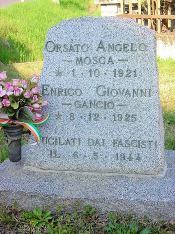 Cippo commemorativo per Orsato e Enrico, con un omaggio floreale e decorazioni simboliche.