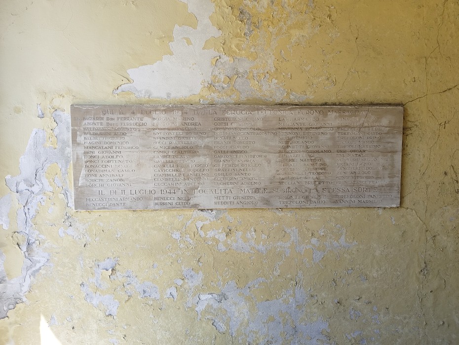 Lapide in marmo con lungo elenco di nomi, fissata a una parete scrostata.