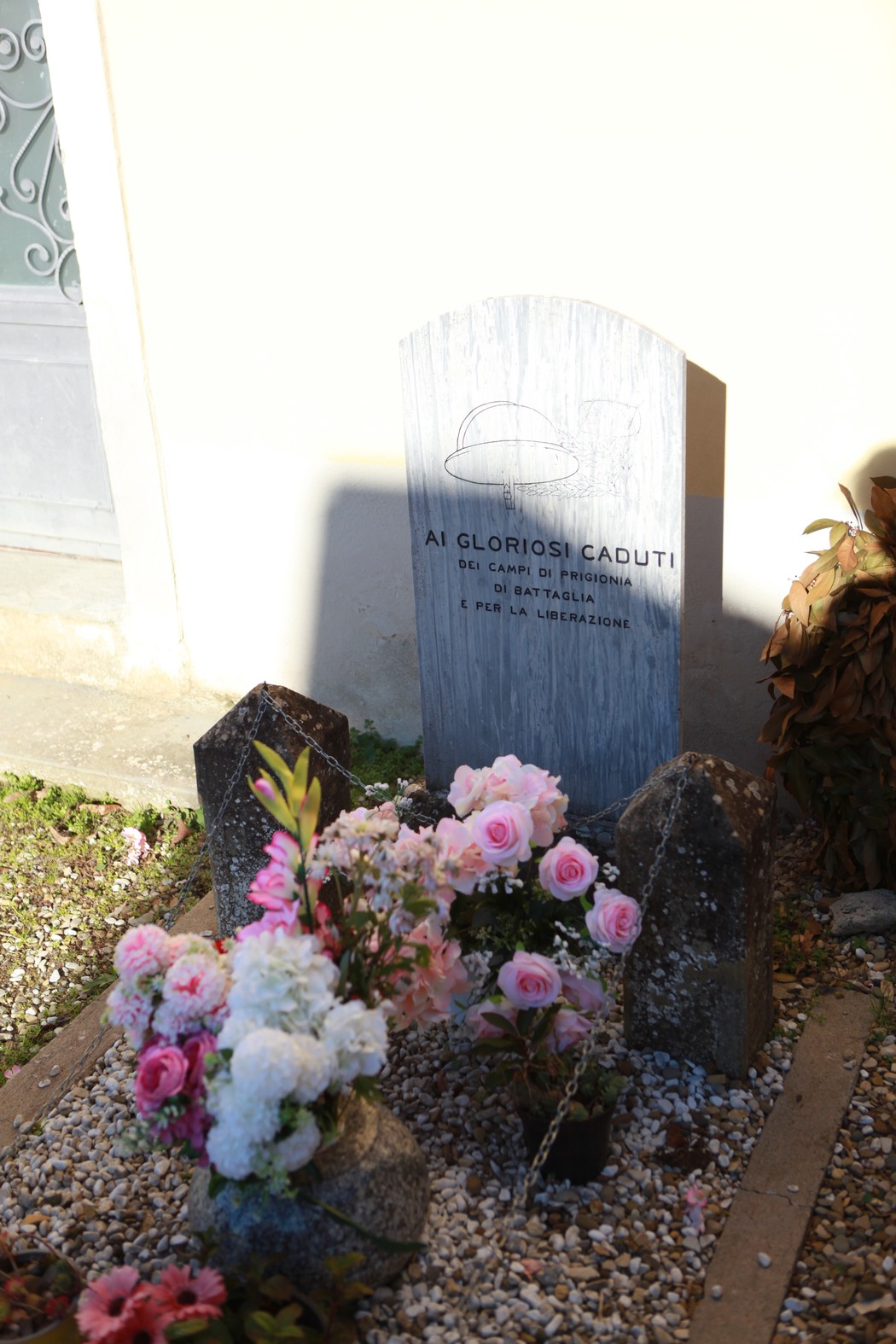 Cippo commemorativo ai caduti, adornato con fiori, in segno di rispetto e memoria.