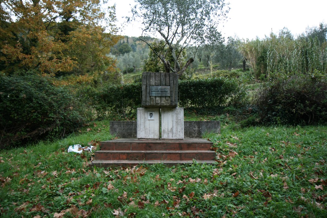 Monumento a Santini immerso nella natura, con gradinate e un albero, circondato da foglie autunnali.