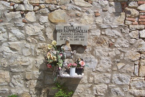 Lapide commemorativa dedicata a Raggioli e Manzardo, con fiori e messaggi di ricordo sulla parete di pietra.