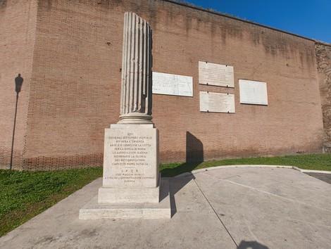 Cippo commemorativo dedicato ai caduti nella difesa di Roma, con architettura classica e scritte di omaggio.