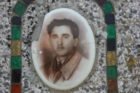 Cippo commemorativo decorato con una fotografia in ceramica di un uomo in posa formale.