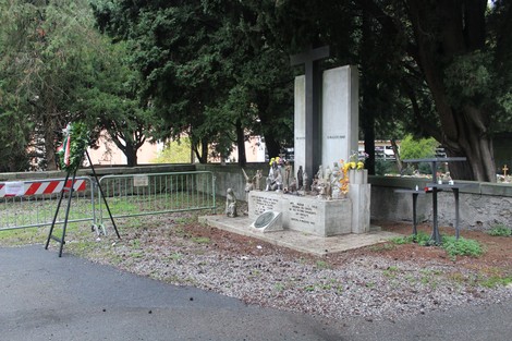 Monumento alle vittime civili con croce e statue, circondato da alberi e aree fiorite. Ambiente opaco e rispettoso.