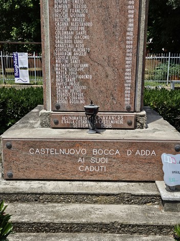 Monumento ai Caduti di Castelnuovo Bocca d'Adda, commemorazione con nomi incisi e decorazioni florali circostanti.