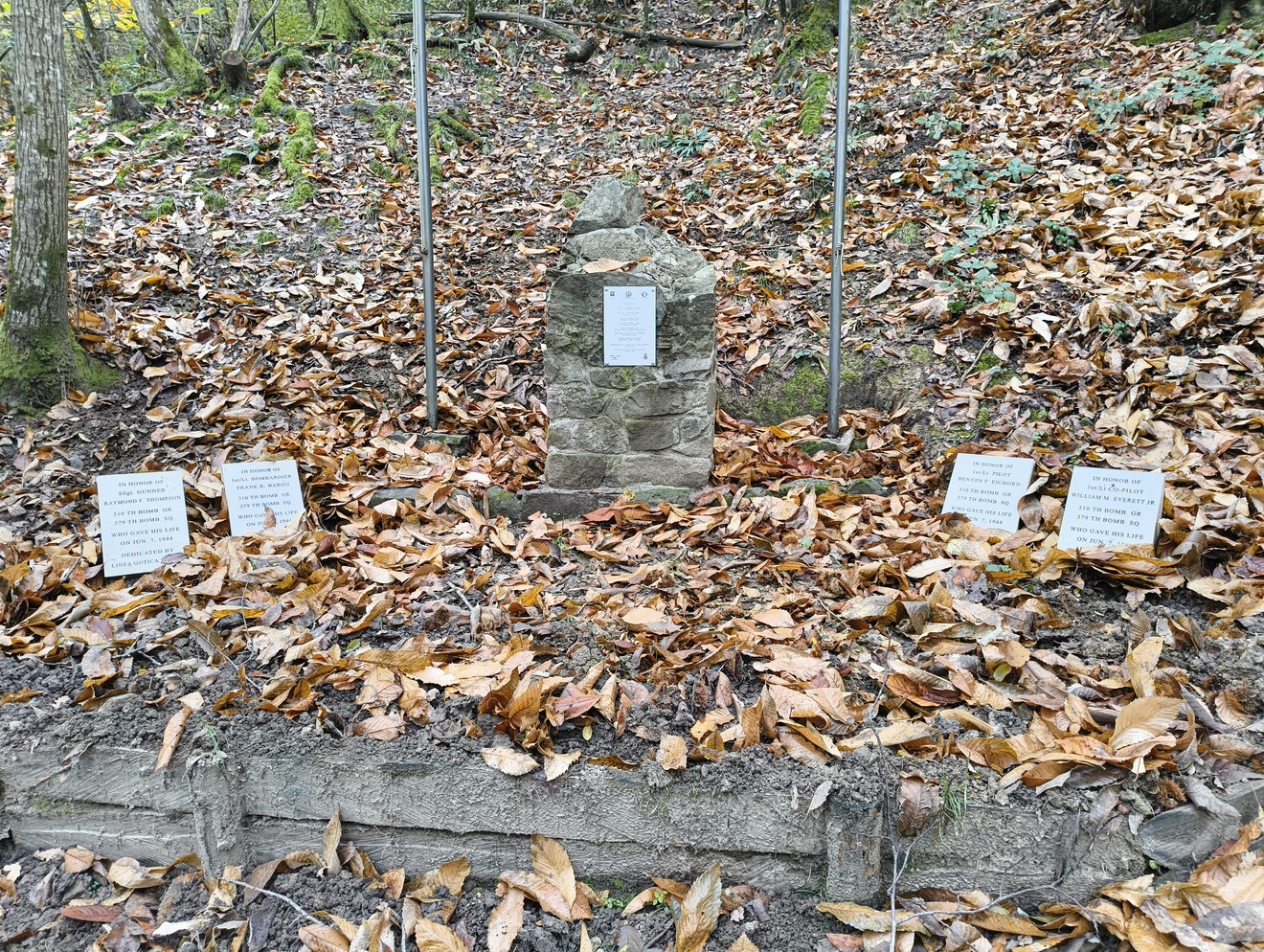Monumento commemorativo dedicato all'equipaggio del B25J, circondato da foglie autunnali.