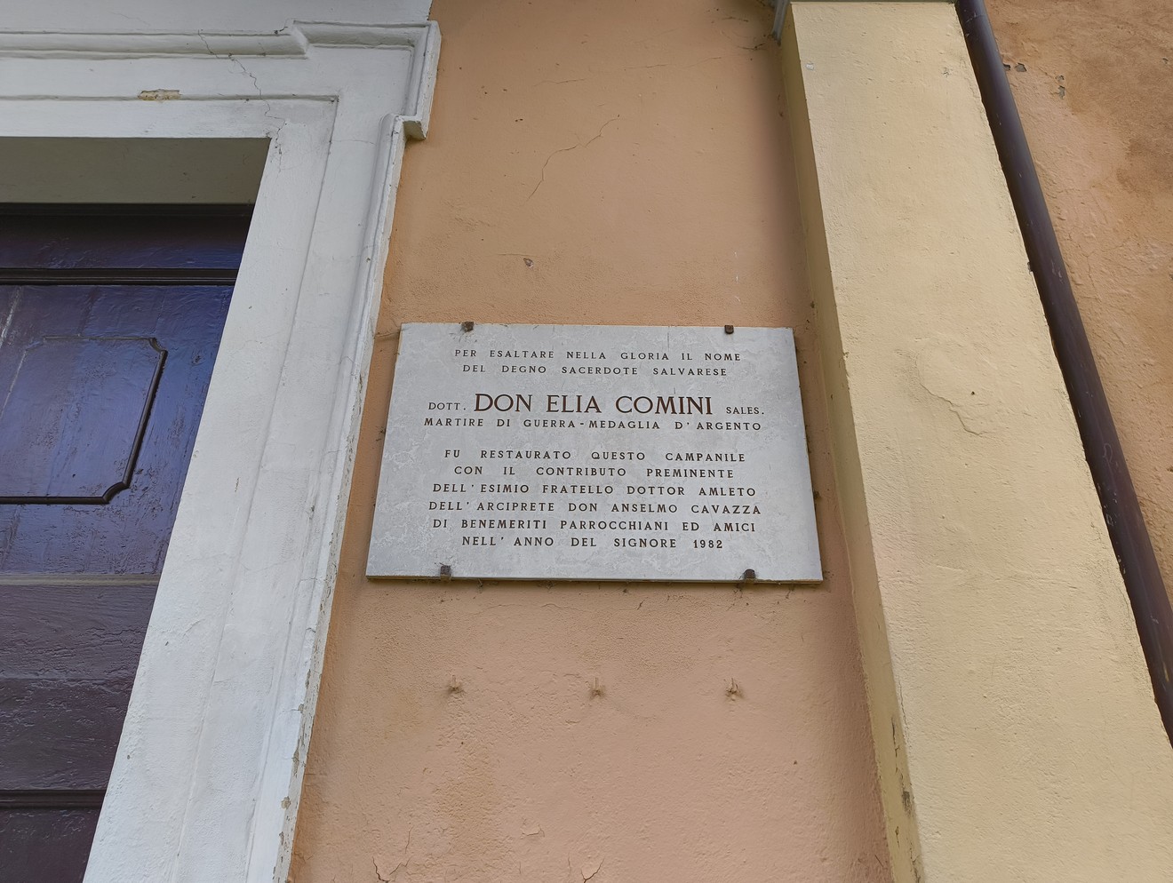 Lapide commemorativa dedicata a Don Elia Comini, martire della guerra, situata su un edificio.