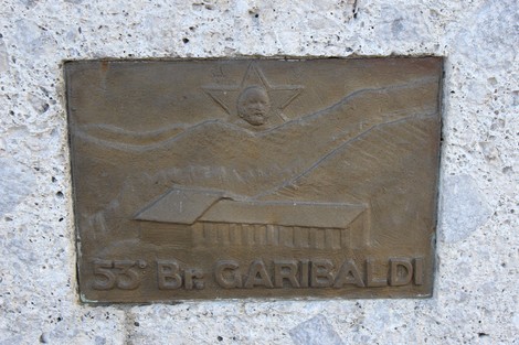 Monumento ai Tredici Martiri, dedicato ai caduti, con rilievi commemorativi e paesaggio montano.