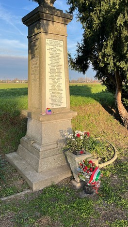 Monumento ai caduti dell'Amola con fiori e un'atmosfera serena nel paesaggio circostante.