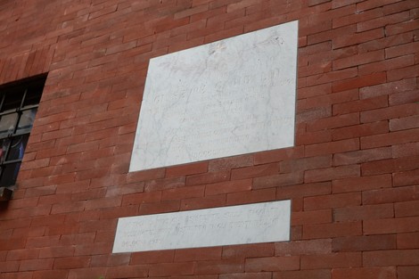 Lapide bianca su un muro di mattoni rossi, dedicata alla ricollocazione della memoria.