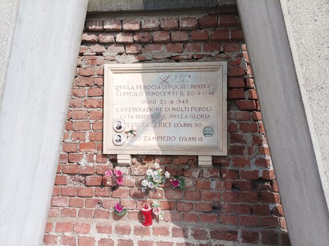 Monumento commemorativo a Clerici e Zampiero, con iscrizioni e fiori sulla parete in mattoni.