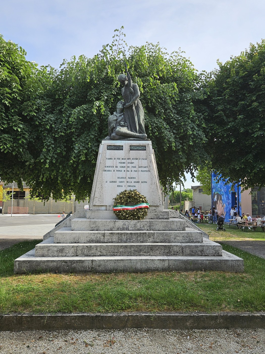 Il Monumento ai Caduti di Solarolo Rainerio, con statue e una corona d'alloro, immerso nel verde.