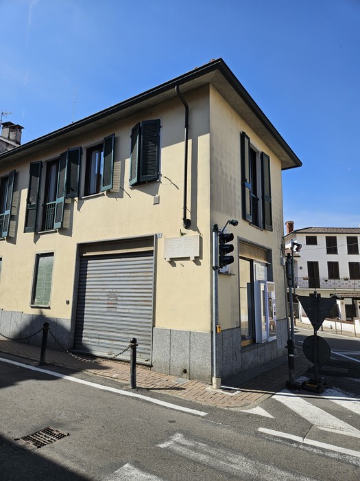 Lapide con iscrizione sulla facciata di un edificio d'angolo, accanto a una finestra con persiane verdi.
